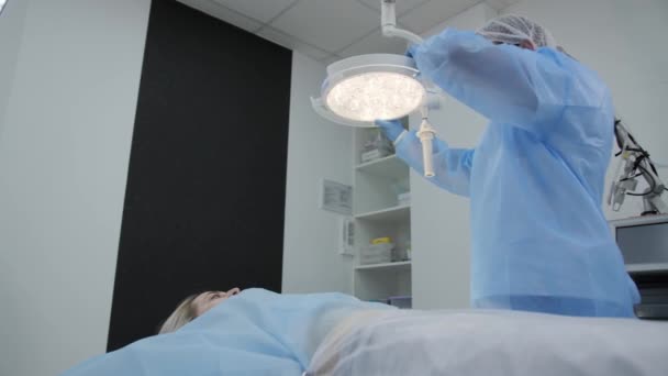 Il chirurgo dirige la lampada verso il paziente e si prepara per un'incisione nell'addome per un'ulteriore liposuzione in sala operatoria. . — Video Stock