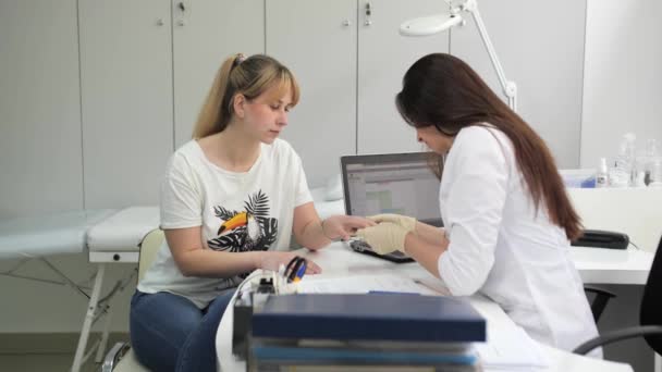 Knappe vrouwelijke dermatoloog onderzoekt de handen van een patiënt in een kosmetologische kliniek. — Stockvideo