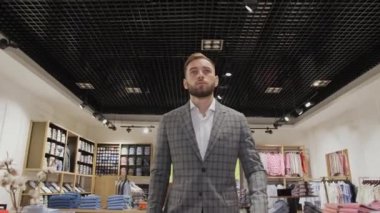 Gri takım elbiseli bir işadamı mağazanın arka planındaki erkek giyim mağazasına giriyor..