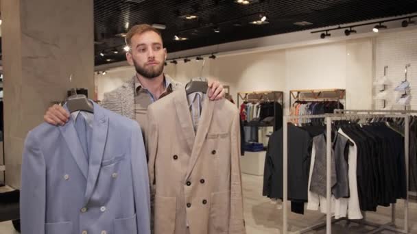 Stilvoller Mann mit Bart wählt Jacke in Herrenbekleidungsgeschäft. — Stockvideo