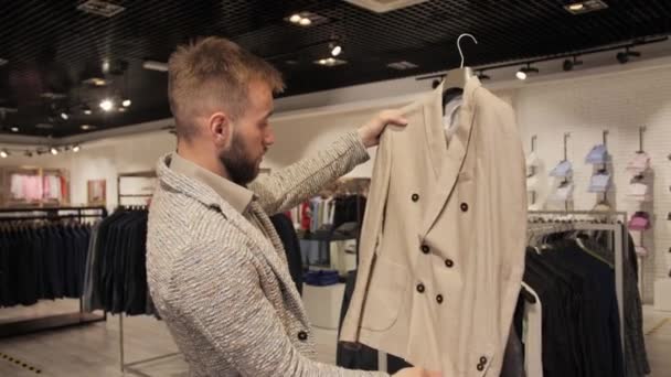 Stijlvolle zakenman met een baard kiest voor een jas in een herenkledingwinkel. — Stockvideo