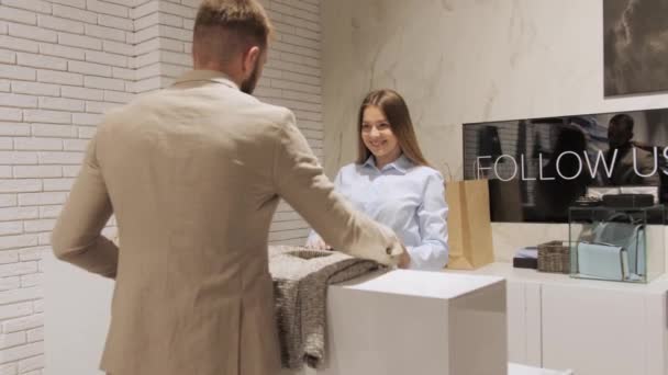 Stylish man in a suit with a beard puts a jacket at the checkout to buy, a sales consultant smiles at him. — Stock Video