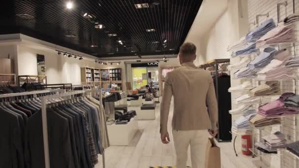 Tevreden klant na het winkelen met een tas in zijn handen verlaat de winkel van merkkleding. — Stockvideo