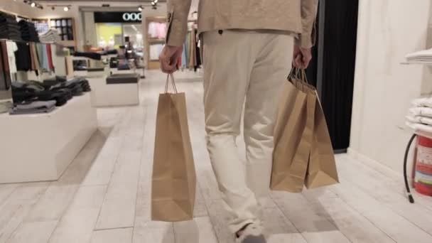 Spokojen klient po nakupování s taškou v ruce opouští sklad značkového oblečení. — Stock video