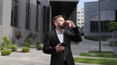 Sakallı yakışıklı bir işadamı sabah kahvesini içerken gözlerini kapar ve iş merkezinin arka planındaki telefona bakar..
