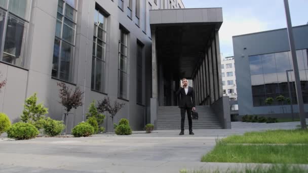 Jonge zakenman in gesprek aan de telefoon op de achtergrond van een modern gebouw bankmedewerker praten aan de telefoon buiten business center. — Stockvideo