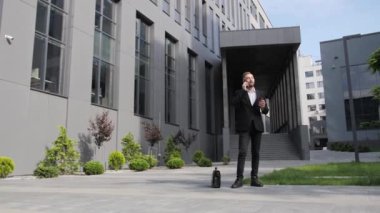 Evrak çantalı yakışıklı bir ofis çalışanı sabah kahvesini içiyor ve iş merkezinde telefonla konuşuyor..