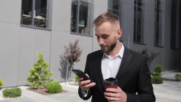 Knappe zakenman met baard drinken 's morgens koffie sluit ogen en kijkt naar telefoon typen bericht op business center achtergrond. — Stockvideo