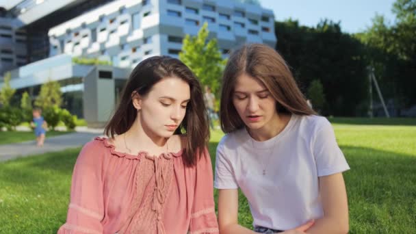Two pretty female students are studying a lecture remotely on a laptop outdoors on the background of modern building. — Stock Video