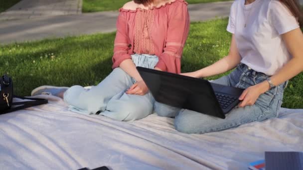 Twee mooie vrienden studeren een lezing op afstand op een laptop buiten op de achtergrond van een modern gebouw. — Stockvideo