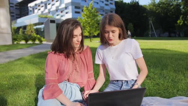 Dois amigos bonitos estão estudando uma palestra remotamente em um laptop ao ar livre no fundo do edifício moderno . — Vídeo de Stock