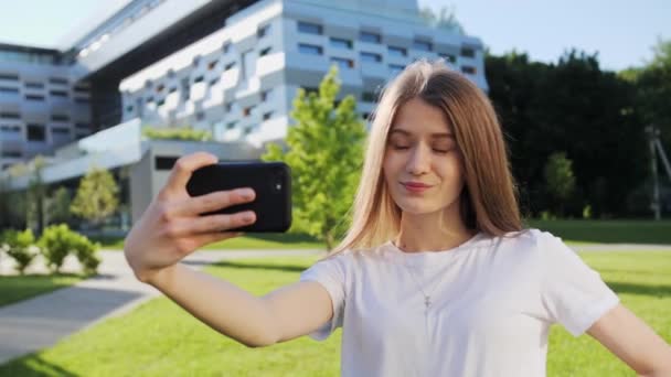 Menina bonita falando em videochamada com um amigo no fundo de um edifício moderno. Verão dia ensolarado . — Vídeo de Stock