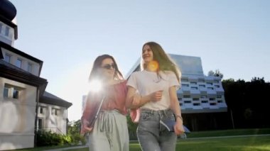 Dizüstü bilgisayarı ve defteri olan iki kız arkadaş üniversiteden ayrılıp gülüyor..