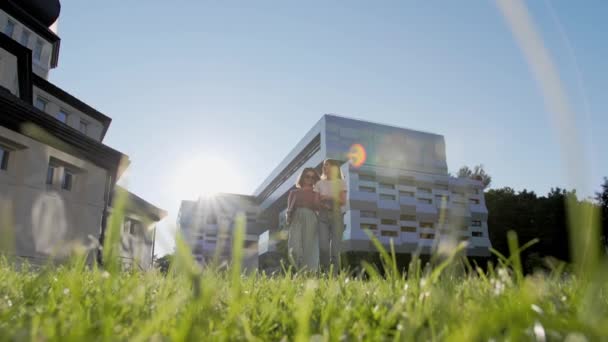 Twee studenten met een laptop en een notebook gaan van de universiteit en lachen. — Stockvideo