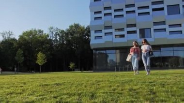 İki neşeli kız arkadaş üniversiteden ayrılıp gülüyor..