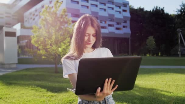 Ragazza carina e carismatica con l'apparecchio che lavora su un computer portatile all'aperto e sorridente. — Video Stock