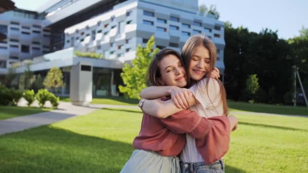 Dua pacar perempuan yang lucu memeluk di luar ruangan di latar belakang bangunan modern persahabatan gadis-gadis musim panas. — Stok Video