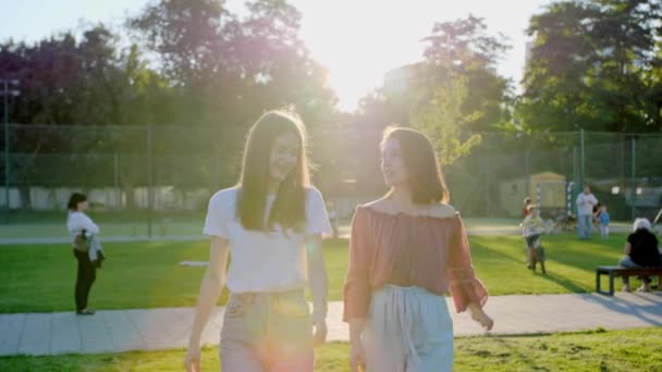 Two best beautiful friends walk in the park and have fun against the back light. — Stock Video