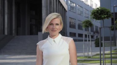 Kendine güvenen güzel bir iş kadınının portresi kameraya bakıyor ve modern binanın arka planında poz veriyor. İş elbisesi sarışın kız. Başarılı Kadın.