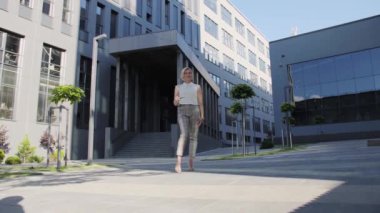 Takım elbiseli çekici bir sarışın modern bir ofis merkezinin arka planında siyah çerçeveli gözlüklerini çıkarıyor. Sarışın Kız. Başarılı Kadın.