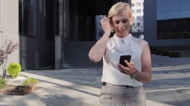 Beyaz tişörtlü güzel ve kendine güvenen sarışın uygulamayı bir cep telefonuna yerleştirir ya da iş arkadaşlarıyla sohbet eder.