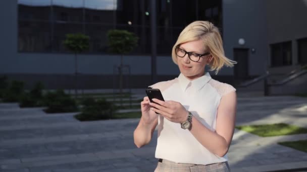 Beautiful blonde in a white shirt makes online shopping on the background of the mall.Successful Woman. — Stock Video