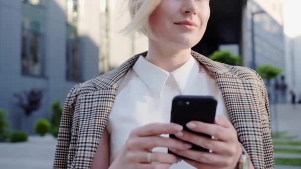 一位穿着商务服装的金发女人的画像，她用手机与同事们在户外交流. — 图库视频影像
