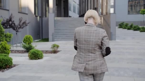 Επιτυχημένη ξανθιά επιχειρηματίας πάει στη δουλειά και μιλάει σε ένα κινητό τηλέφωνο. Ντυμένος με επαγγελματικό κοστούμι με όμορφα χτενισμένα μαλλιά. — Αρχείο Βίντεο