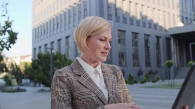 İnternet kamerasında konuşan çekici sarışın kadın ofis merkezinin arka planında dizüstü bilgisayar kullanıyor. İş kadını video görüşmesinde konuşurken gülüyor..