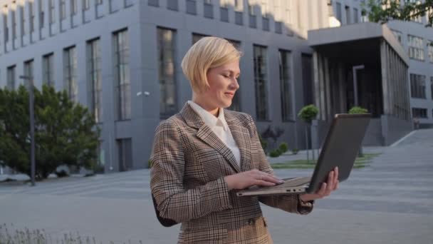 Schöne blonde Frau spricht auf Webcam mit Laptop im Freien auf Büro-Center-Hintergrund. — Stockvideo