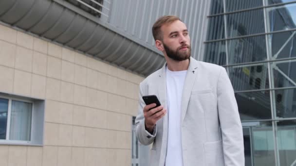 수염을 기른 세련 된 사업가가 공항에 가서 이동 전화를 사용 한다. 밝은 재킷과 흰색 티셔츠를 입고 여행하는 사업 스타일, 현대 생활 방식. 활동적 인 생활. — 비디오