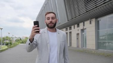 Sakallı genç işadamı ortaklarıyla yaptığı bir video konuşmasında konuştu. Hafif modern bir takım elbise ve beyaz bir tişört giymişti. Ofis merkezinin arka planı