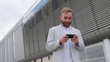 Sakallı yakışıklı bir adam dışarıda cep telefonuyla poker oynuyor ve kazanmaktan mutlu. Şık bir ceket, mobil uygulama, sosyal ağlar. Oyun oyna..