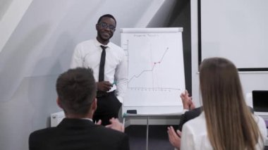 Seyirci, Koyu tenli Afro-Amerikan işadamının konferans odasında bir rapor hazırlamasını ve şirketin kârını analiz etmesini alkışlıyor. Takım çalışması kavramı..