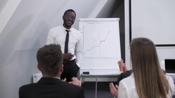 Publiken applåderar mörkhyade afro amerikanska affärsman gör en rapport i ett konferensrum och analyserar företagets vinst. Begreppet lagarbete. — Stockvideo