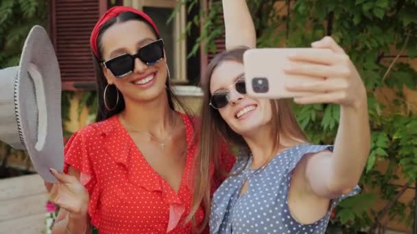 İki en iyi arkadaş eğleniyor, gülüyor, kentte çiçekli güzel bir evin arka planında selfie çekiyor.. — Stok video