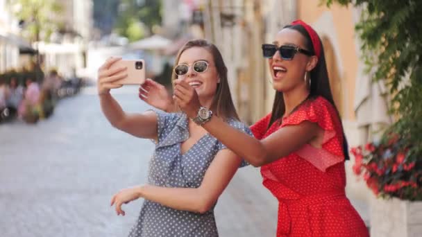 Zwei fröhliche und glückliche attraktive Freundinnen in Sommerkleidern machen Selfies. Telefonmädchen draußen. — Stockvideo