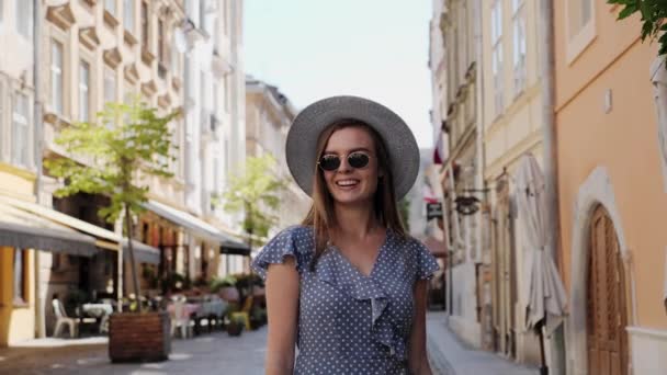 Menina elegante e bonita em óculos de sol e um chapéu andando na rua da cidade, onde um monte de cafés e risos . — Vídeo de Stock