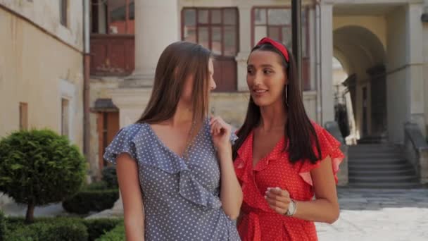 Twee stijlvolle vriendinnen in zomerjurken delen hun geheimen op straat. Vriendschap van meisjes buiten. — Stockvideo