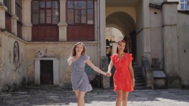 İki turist arkadaş el ele tutuşup gülüyor ve Avrupa 'nın eski şehrinin arka planında yürüyorlar..