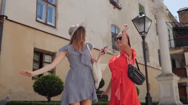 Två bästa vänner i solglasögon och sommarklänningar lekfullt dansa och ha kul i Barcelona. Blond och brunett. — Stockvideo