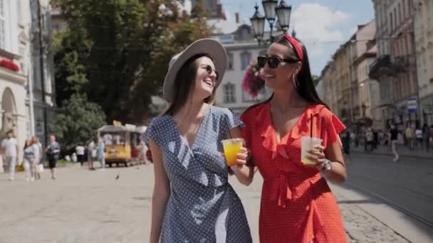 Deux filles avec de la limonade marchant dans la rue urbaine pleine de gens et de cafés. — Video