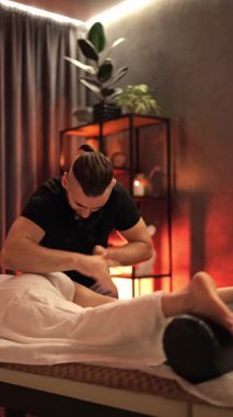 Masör, sakin bir kaplıca ortamında rahatlamış bir bayan müşteriye terapatik bacak masajı sağlar. Siyahlar içindeki uzman, sağlığa teşvik ediyor, masaj masasında rahatlık ve derin bir rahatlama sunuyor..