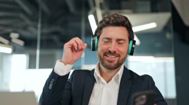 Koyu takım elbiseli ve beyaz gömlekli profesyonel iş adamı modern bir ofiste kulaklıkla müzik dinliyor ve keyifli bir anın tadını çıkarıyor..