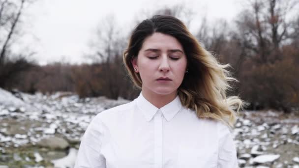 Девушка закрывает глаза в белой рубашке на скалистой снежной реке. Лицо спокойствие лицо 4K . — стоковое видео