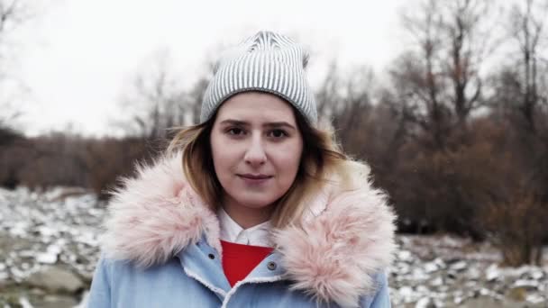 Retrato niña sonriente cara mira a la cámara en el sombrero con el viento helada bosque del norte 4K — Vídeos de Stock