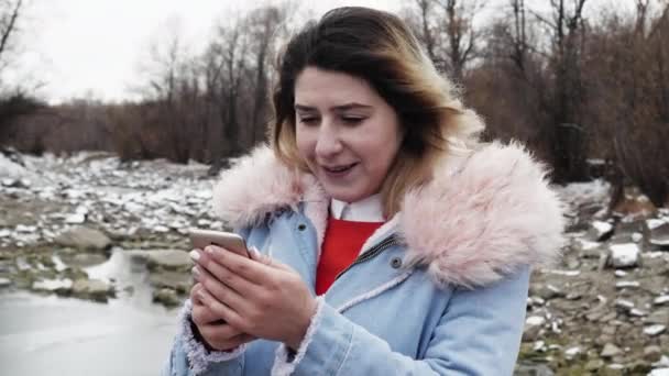 Chica chateando SMS mensaje en el móvil en el valle del bosque del norte con viento helado 4K — Vídeo de stock
