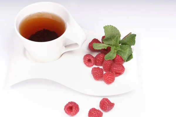 cup of black ceylon tea with raspberries and sprigs of mint on wavy white plate