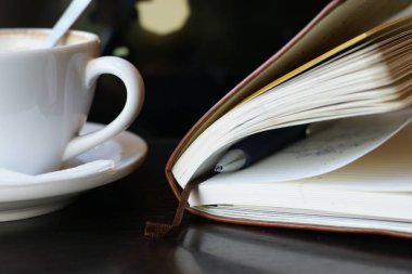 Bir fincan kahve ve masanın üzerinde kalem olan bir defter. 