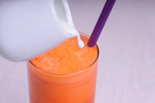 glass of fresh carrot juice with milk on wooden table